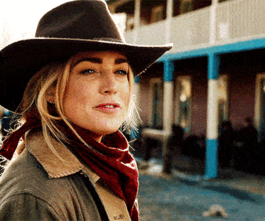 a woman wearing a cowboy hat and scarf looks to the side