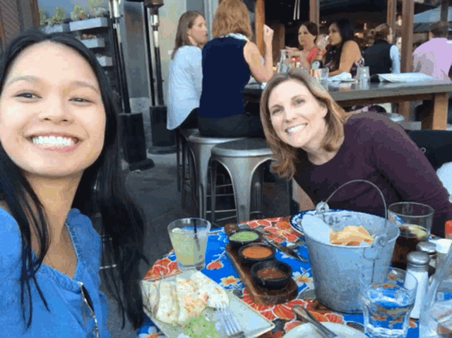 two women are sitting at a table with a bucket of chips on it