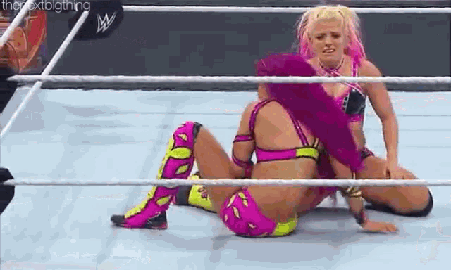 two women are wrestling in a ring and one of them is laying on the floor .