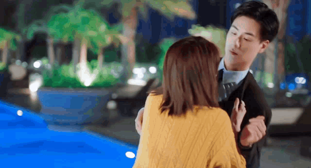 a man and woman are hugging in front of a swimming pool