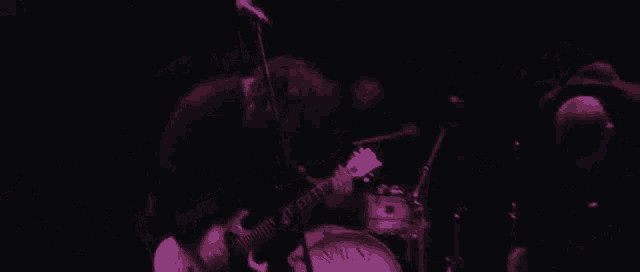 a man is playing a guitar on stage in front of a drum set in a dark room .