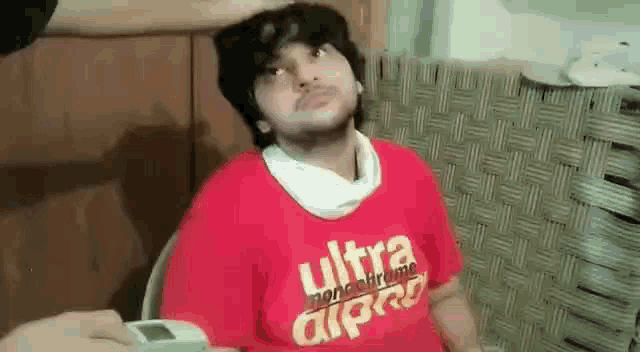 a man wearing a red t-shirt with the word ultra on it is sitting in a chair .