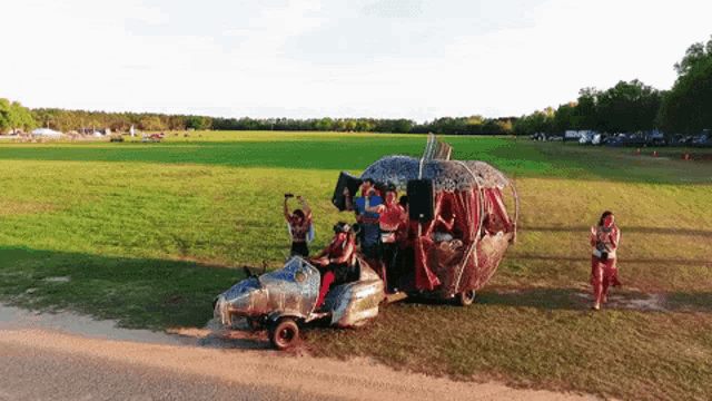 a group of people are standing in a field with a car that looks like a heart on wheels