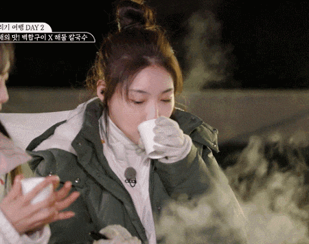 a woman in a green jacket drinking from a white cup with day 2 written on the bottom