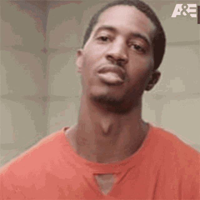 a man in an orange shirt is making a funny face and looking at the camera .