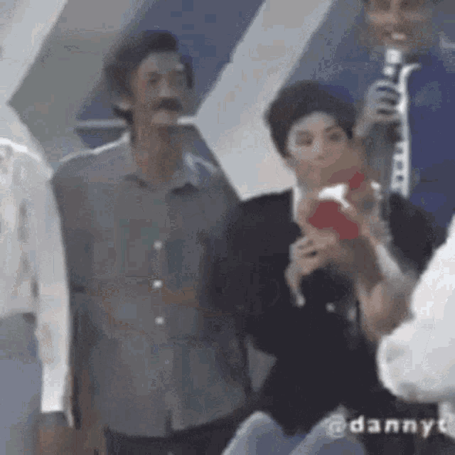 a man with a mustache is talking into a microphone while a woman holds a red box in her hand .