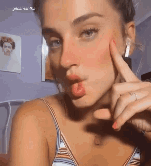 a woman in a striped tank top is making a funny face with her finger in her mouth .