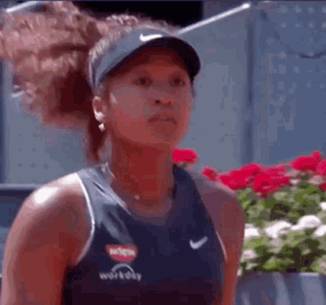 a woman wearing a hat and a tank top is standing in front of flowers .