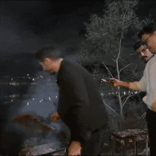 a man in a black jacket is cooking food on a grill at night