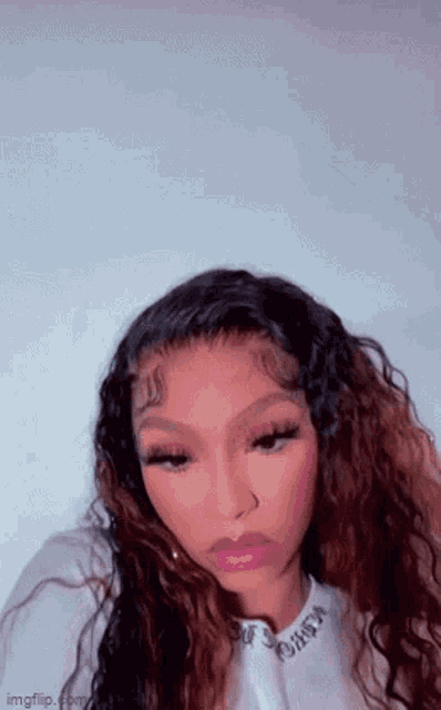 a woman with long curly hair is wearing a white shirt and taking a picture of herself .