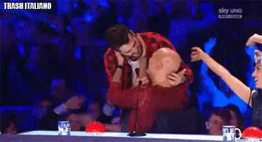 a man is hugging another man in front of a microphone while a woman looks on .