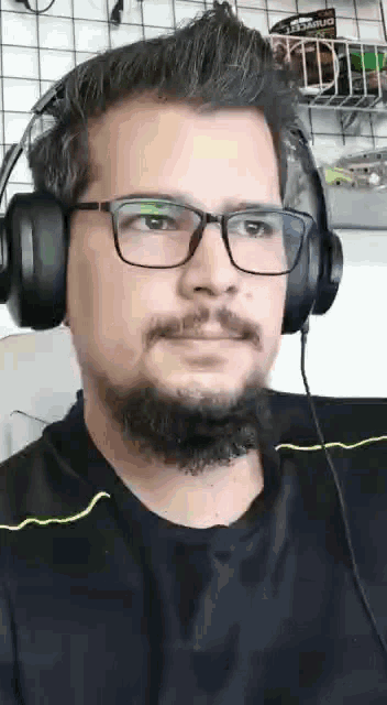a man with glasses and a beard is wearing headphones and looking at the camera .