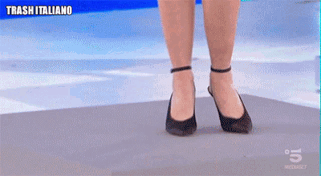 a woman wearing black high heels is walking on a gray surface with trash italiano written on the bottom