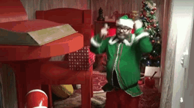 a man dressed as an elf is dancing in a room with a christmas tree in the background