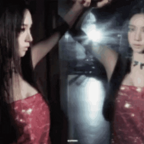 a woman in a red dress is looking at her reflection in the mirror .