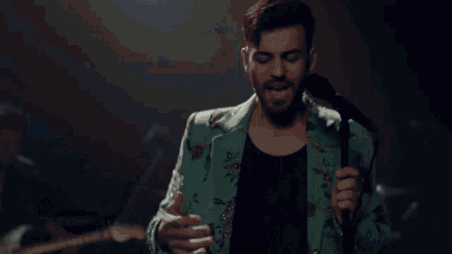 a man in a green jacket is singing into a microphone on a stage with his arms outstretched .