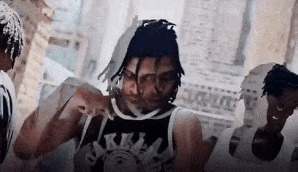 a group of men are standing around a man with dreadlocks wearing a basketball jersey .