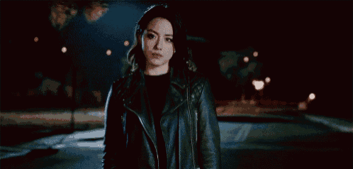 a woman in a leather jacket is standing on a dark street at night .