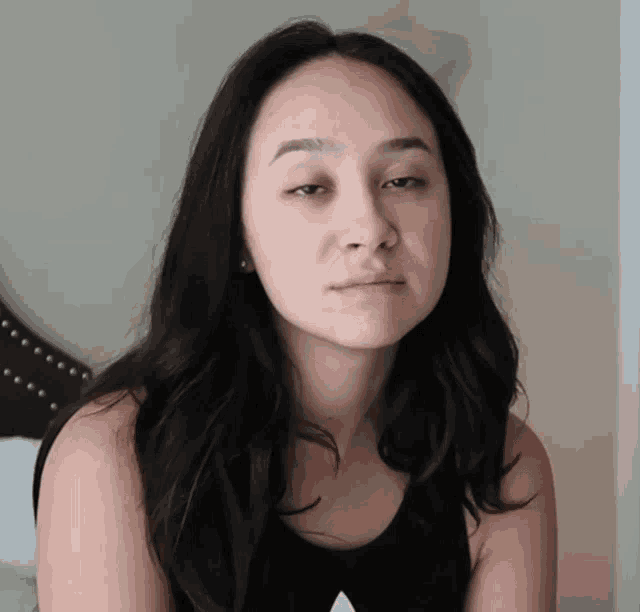 a woman without makeup is sitting on a bed and looking at the camera