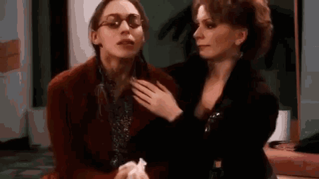 two women are sitting next to each other in a room and one of them is holding a napkin .