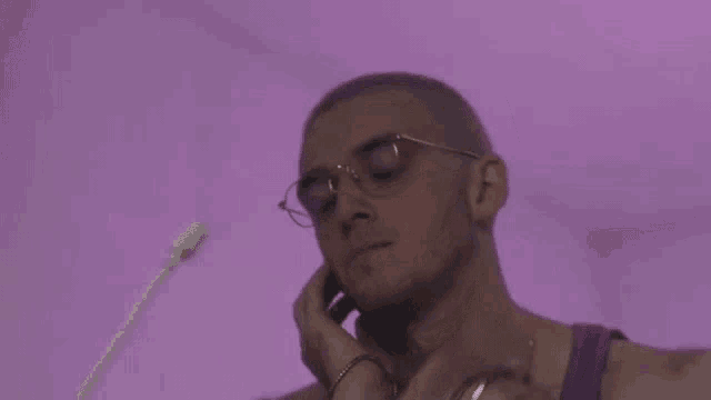 a man wearing glasses and a purple tank top is covering his face with his hands