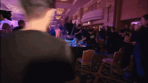 a crowd of people are gathered in a room with a purple light shining on them