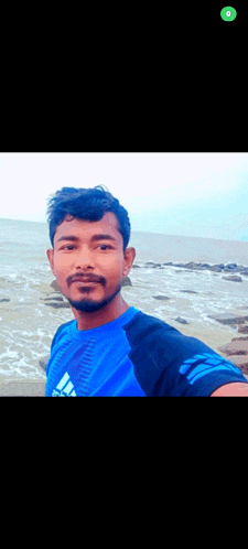 a man in a blue adidas shirt is taking a selfie on the beach