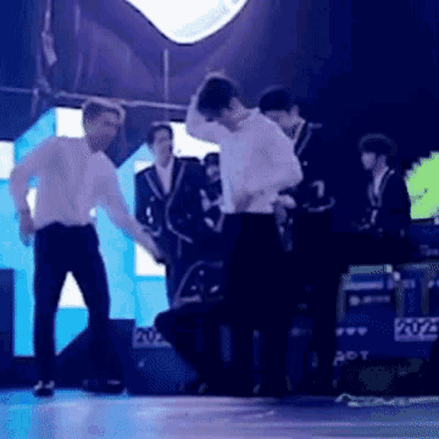 a group of men are dancing on a stage in front of a large screen .