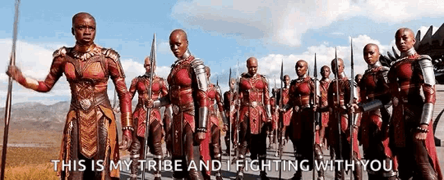 a group of soldiers are marching down a road holding spears and shields .