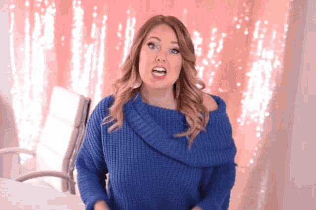 a woman in a blue sweater is standing in front of a pink backdrop