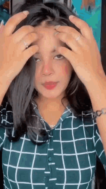 a woman in a plaid shirt is adjusting her hair .