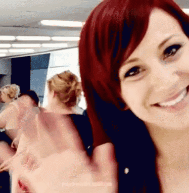 a woman with red hair smiles and waves at the camera