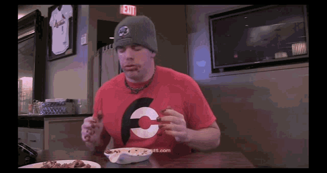 a man wearing a red shirt with the letter c on it sits at a table