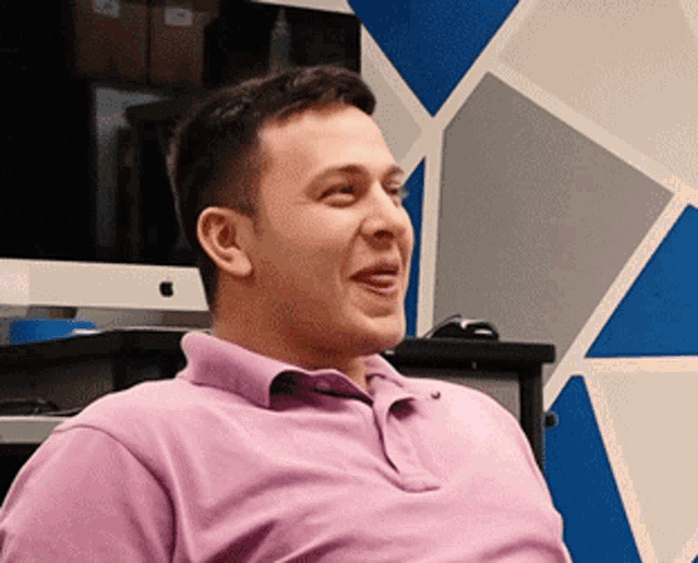 a man in a pink shirt sits in front of an apple computer