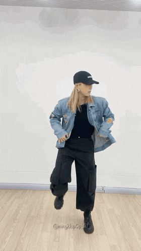 a woman wearing a denim jacket and a black hat is standing on a wooden floor