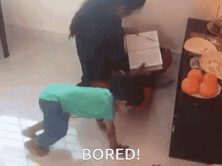 a boy is crawling on the floor while a woman sits at a desk and the word bored is on the bottom of the image