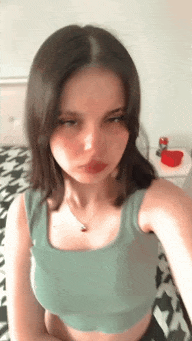 a young woman in a green tank top is taking a selfie in a bedroom .
