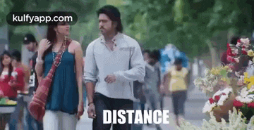 a man and a woman are walking down a street in front of flowers .