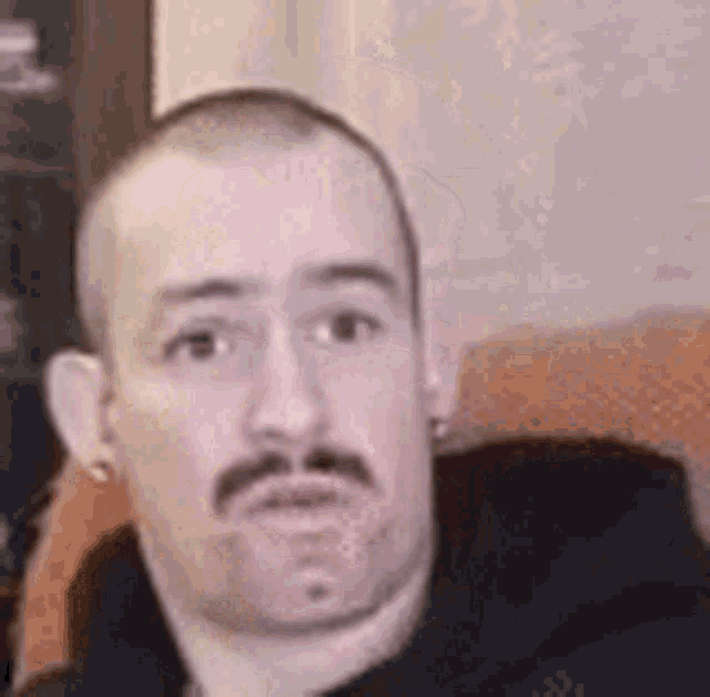 a man with a mustache and a shaved head is sitting in a chair .
