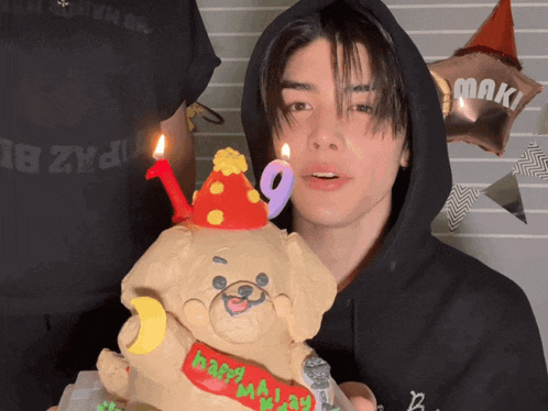 a man in a black hoodie is holding a cake with a teddy bear on it and a number 9 candle