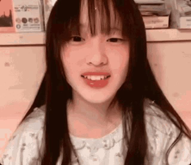 a young girl with long hair and bangs is smiling while looking at the camera .