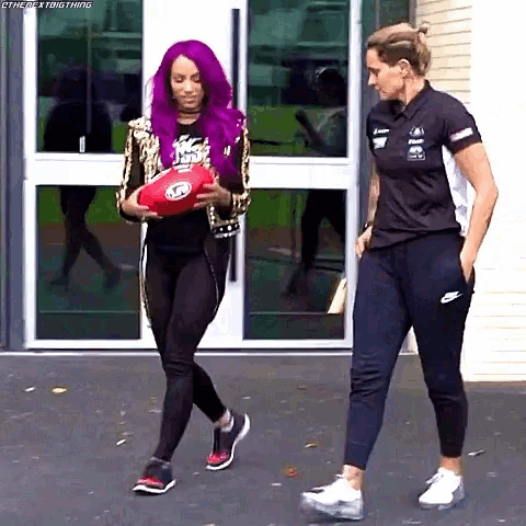 a woman with purple hair is holding a red ball while walking next to a woman in a black shirt .