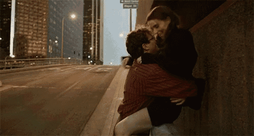 a man is carrying a woman on his shoulders while they kiss on a sidewalk .