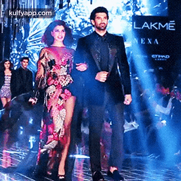a man and a woman are walking down a ramp at a fashion show .