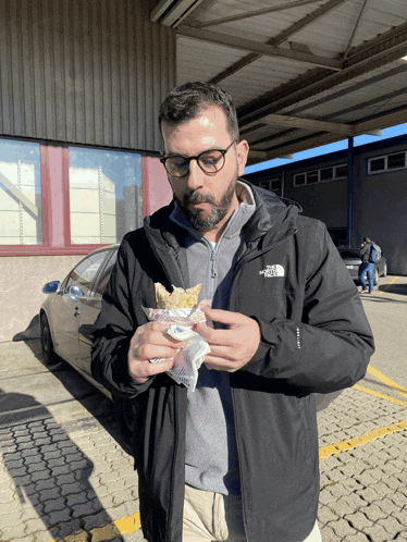 a man wearing a north face jacket is eating a snack