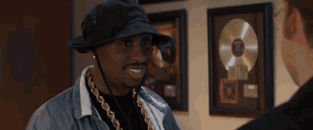 a man wearing a black hat and gold chains laughs