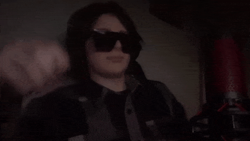 a man wearing sunglasses and a gamelab shirt sits in a dark room