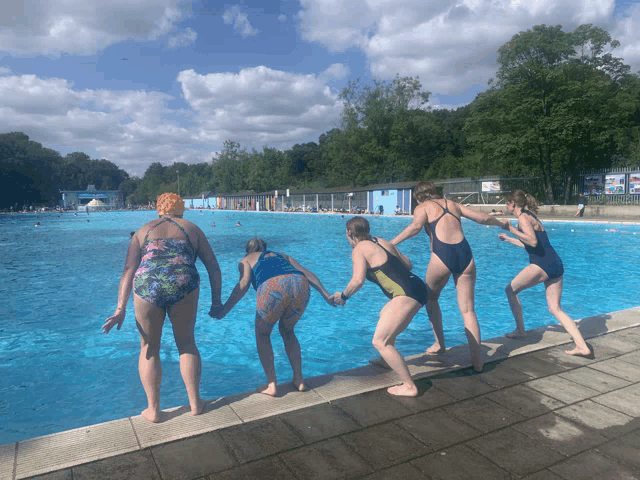 a group of girls in swimsuits are standing on the edge of a pool holding hands