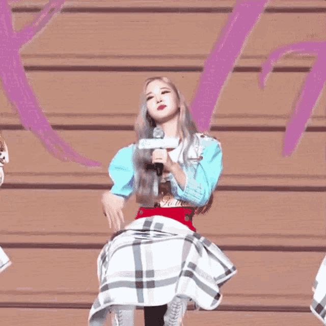 a woman is singing into a microphone while wearing a plaid skirt