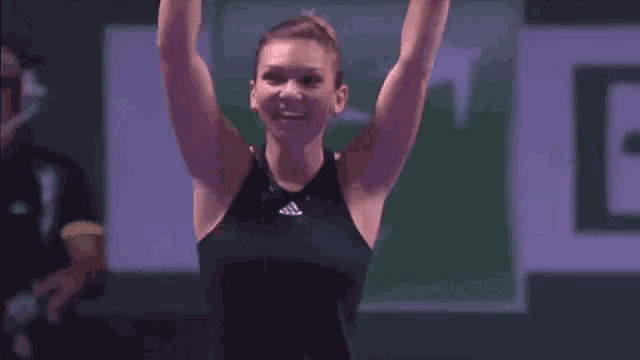 a woman in a black tank top is holding a tennis racket in her hand .